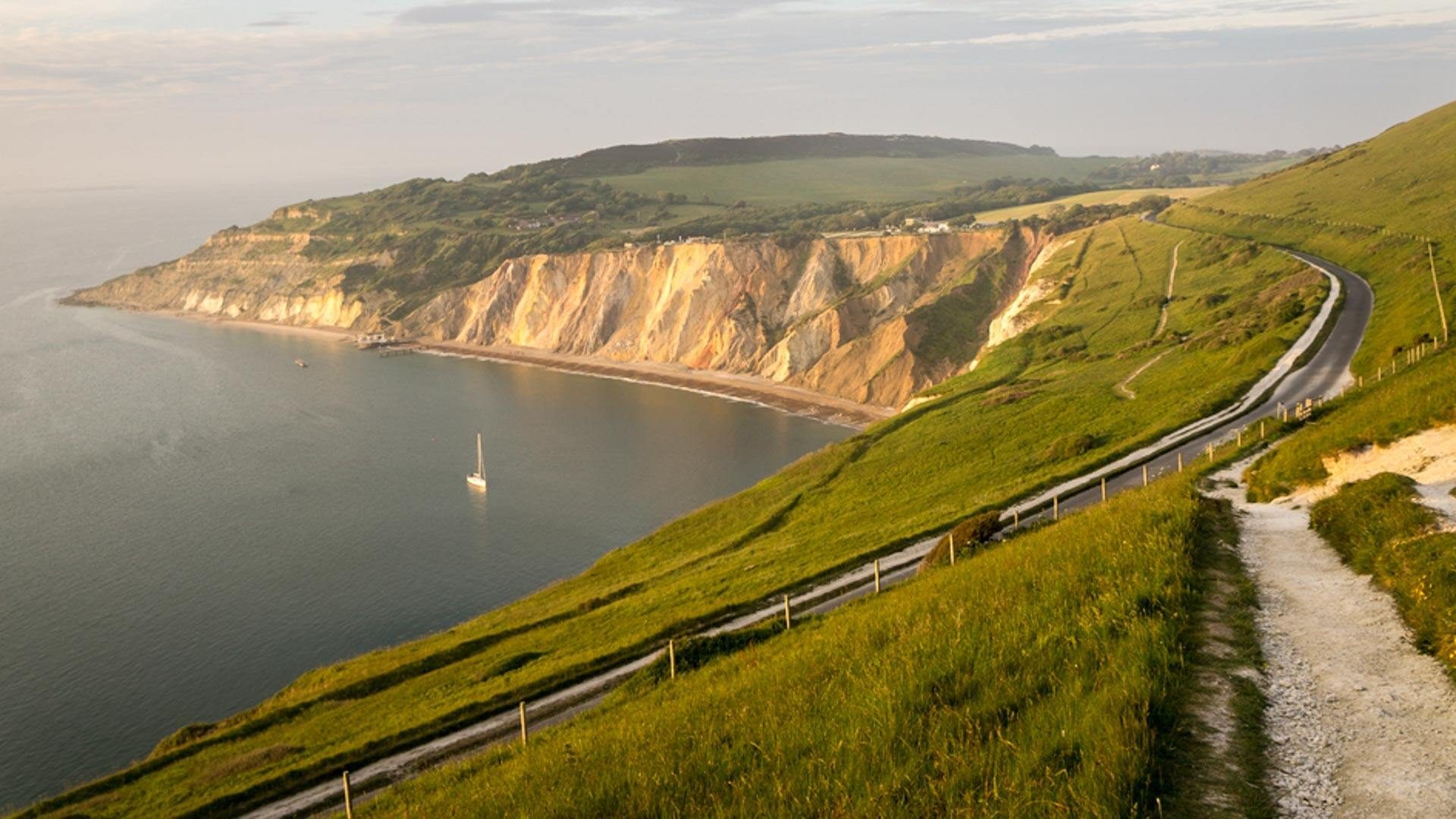 Famous Alum Bay with its coloured cliffs. Road leading along headland with view to Alum bay behind.