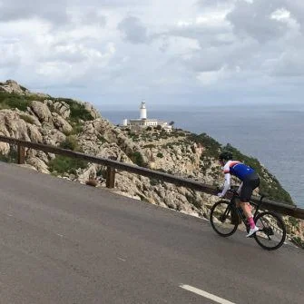 Cyclist cycling the cap de formentor cycling route on Mallorca with lighthouse in distance