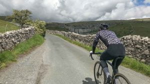 Cyclist cycling past Malham Cove, Yorkshire Dales