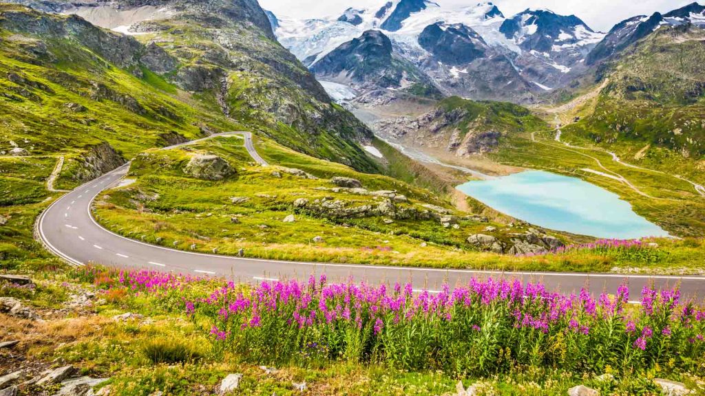 Winding mountain pass road perfect for French Alps cycle tours through gorgeous scenery with mountain peaks, glaciers, lakes and green pastures with blooming flowers in summer
