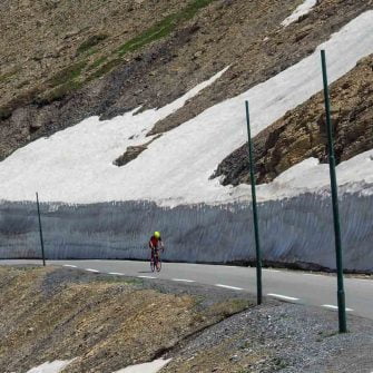 Cyclist on road surrounded by snow in the French Alps