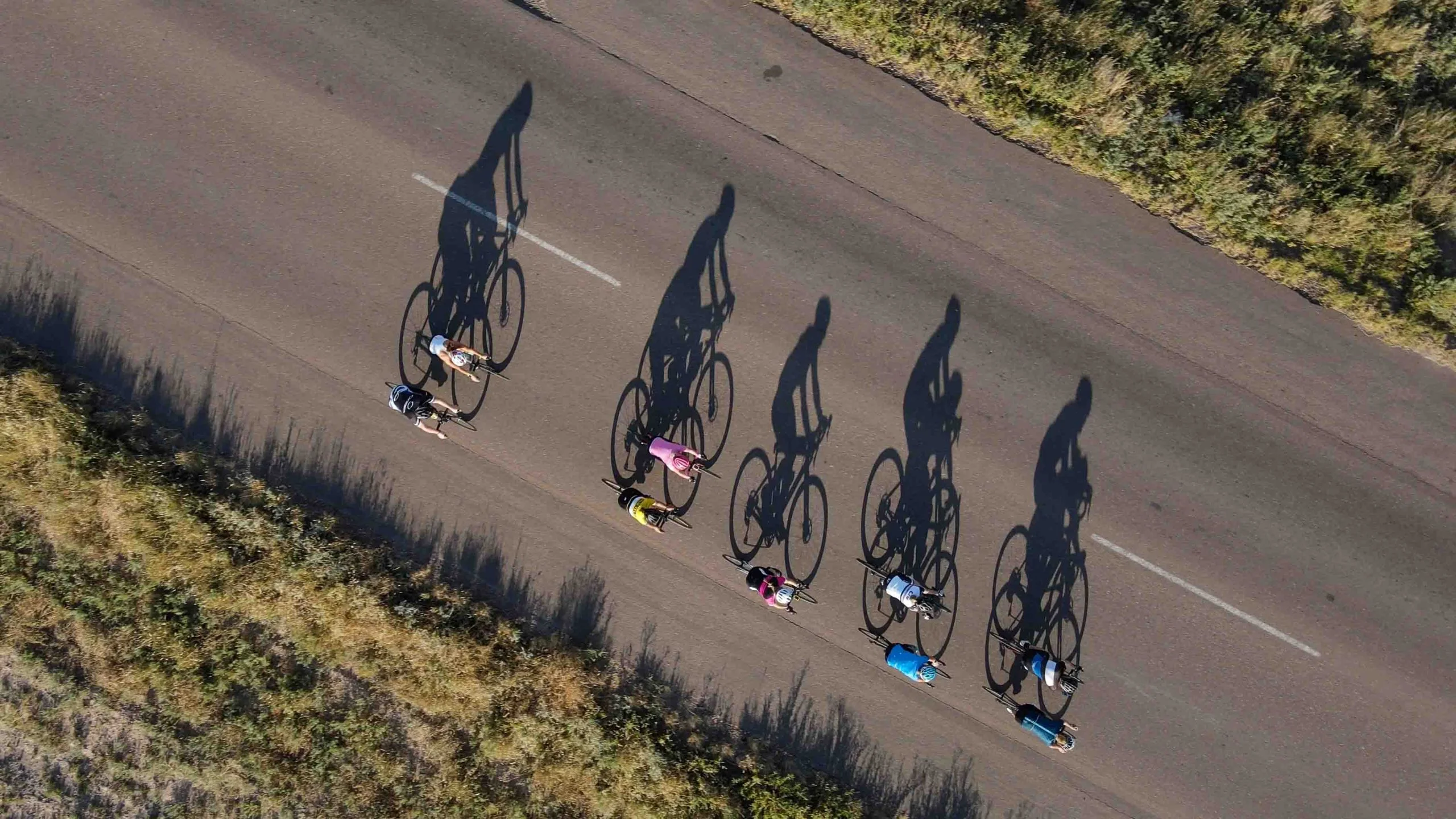 Aerial view of cyclists casting long shadows on the road