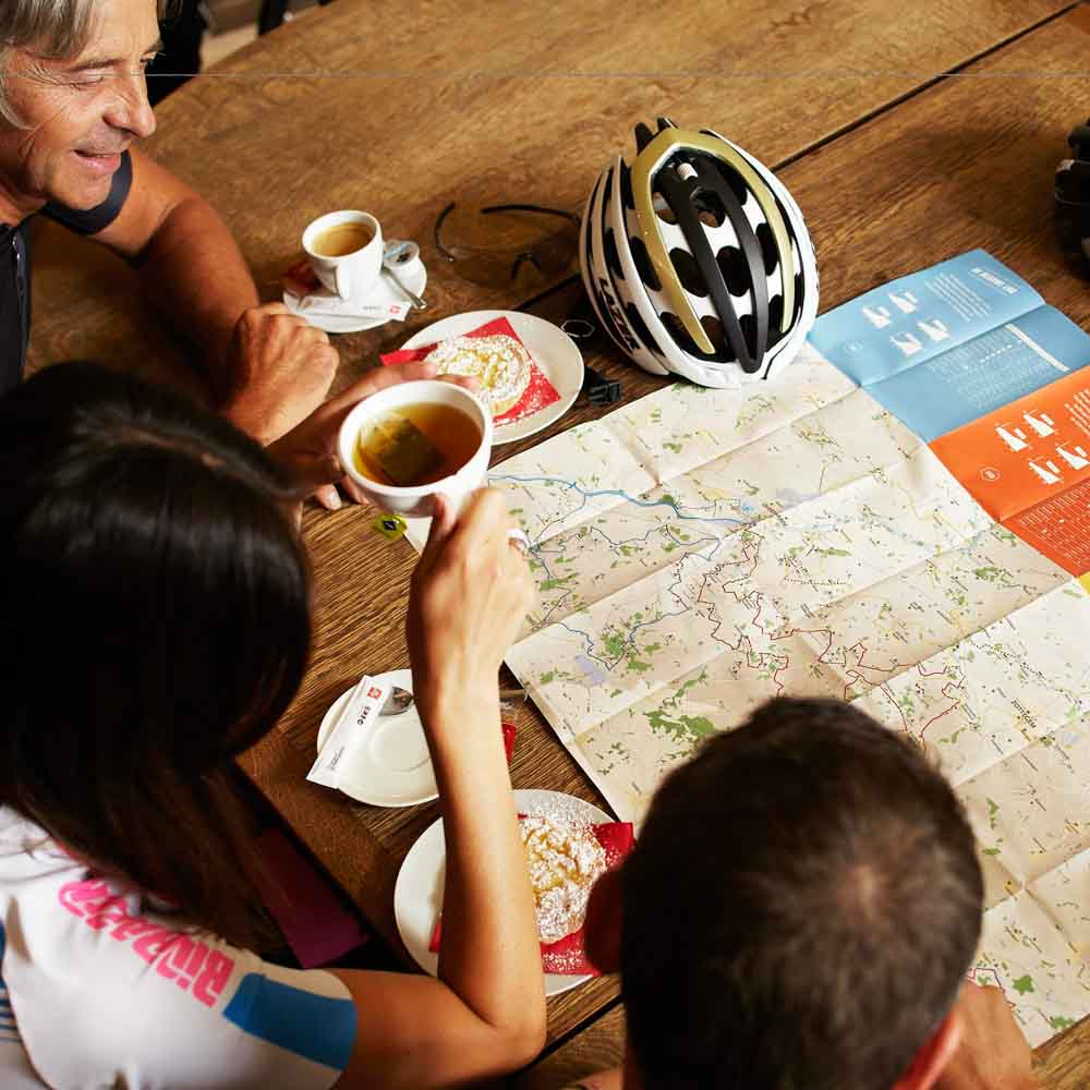 Three cyclists are drinking tea and looking at the map for bike tour in belgium