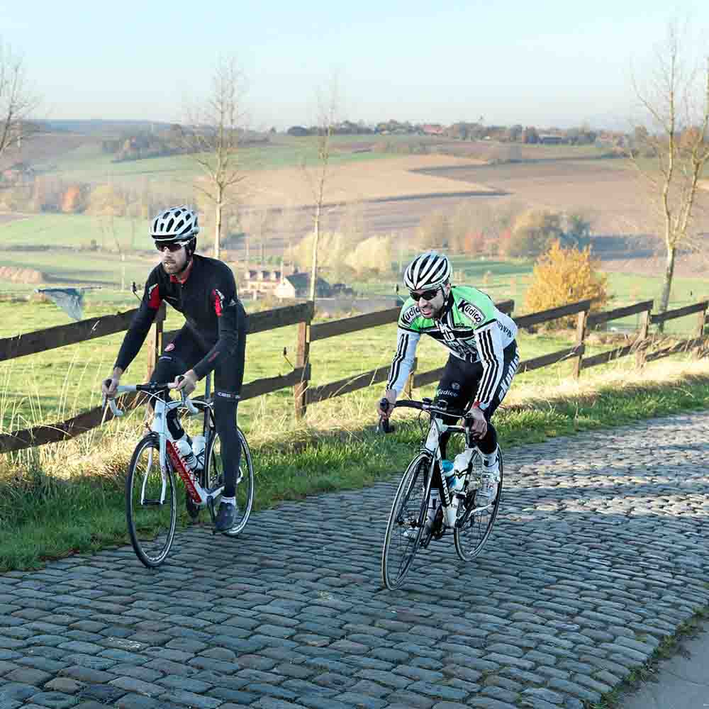 Two cyclists are cycling on the hilly brick road of the village belgium bike tour