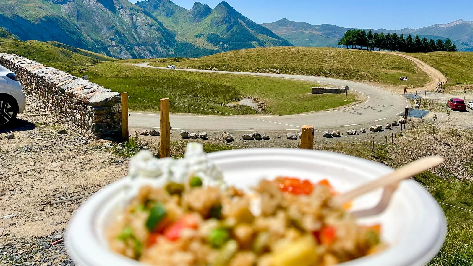 Plate of food at a cycling feed stop with mountain hairpins in the background