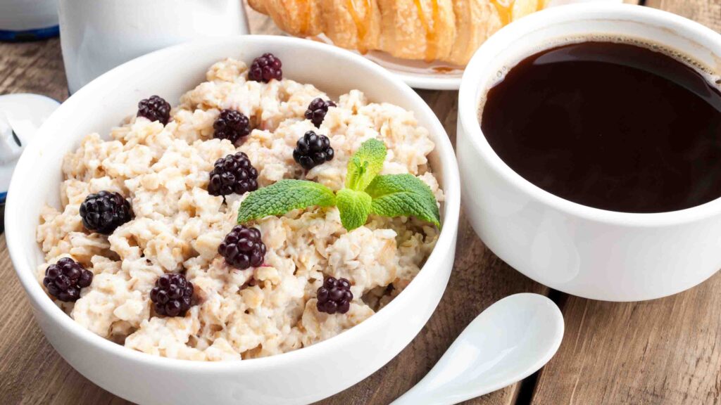Tasty breakfast - oatmeal with berries, milk, coffee cup, croissant with caramel. Oatmeal for healthy breakfast. Closeup
