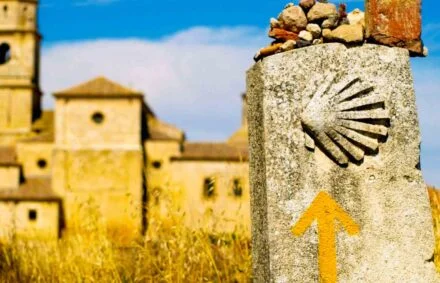 Signpost on Camino de Santiago with scallop shell and arrow and ancient buildings behind
