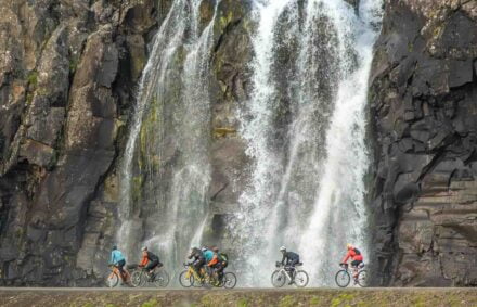 Cyclists pass a waterfall on the Westfjords Way