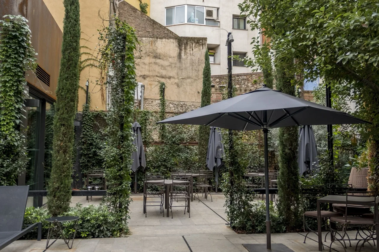 Outdoor area at Hotel Nord 1901 in Girona with chairs, umbrellas, and surrounding trees creating a relaxing space