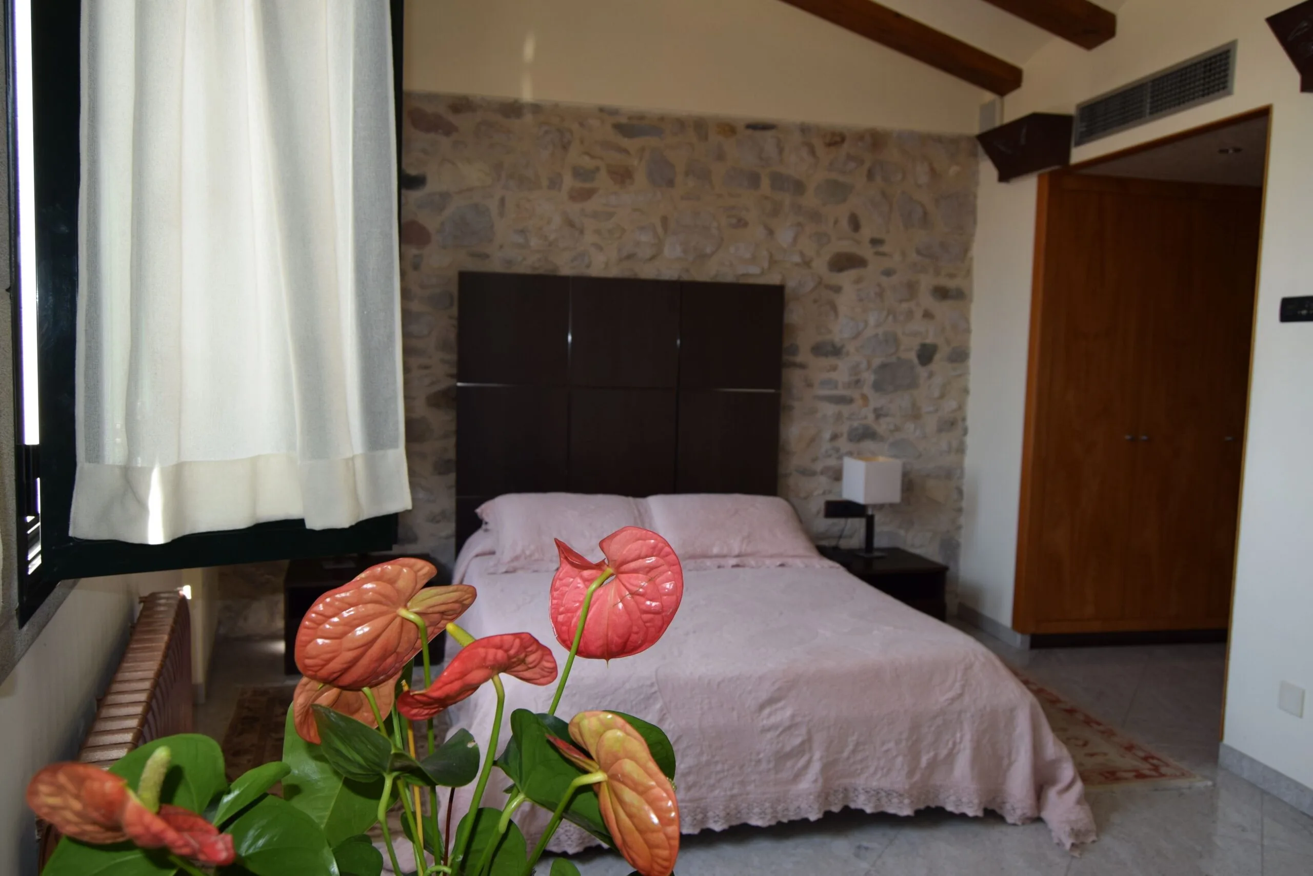 Bedroom at Hotel Històric in Girona with white bed, black headboard, stone accent wall, and white surrounding walls