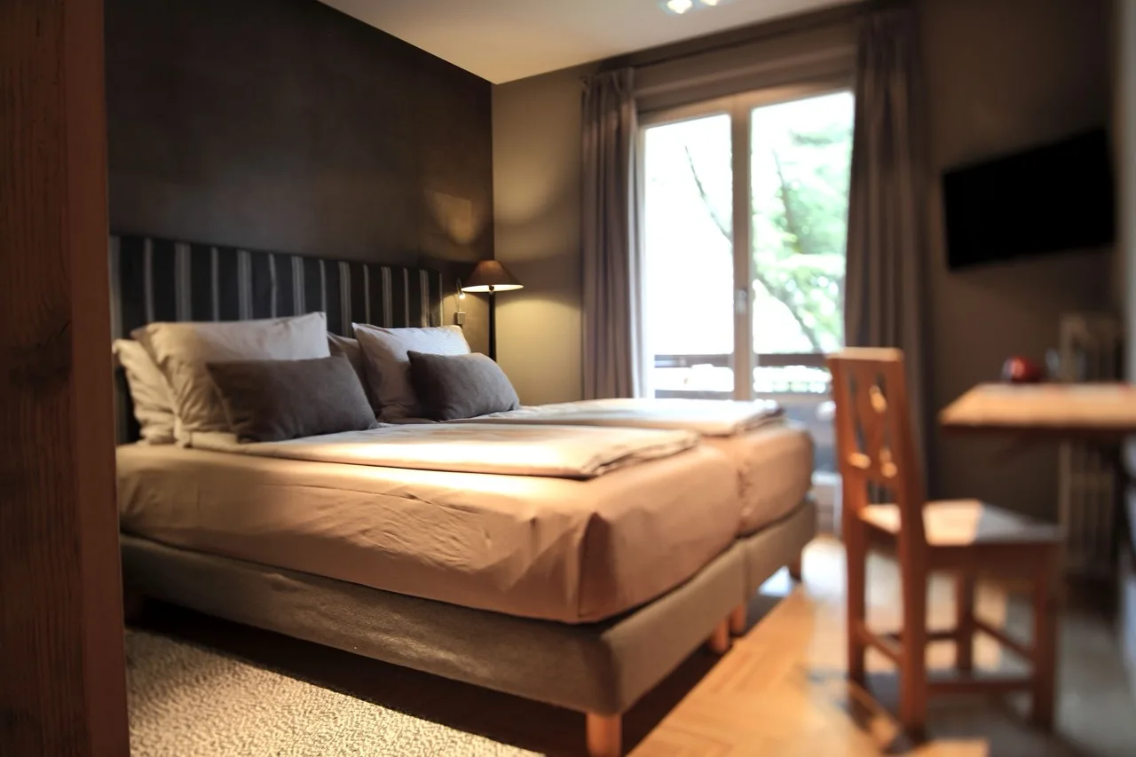 Bedroom at La Genzianella Bormio with twin beds, warm lighting, and balcony view through glass doors