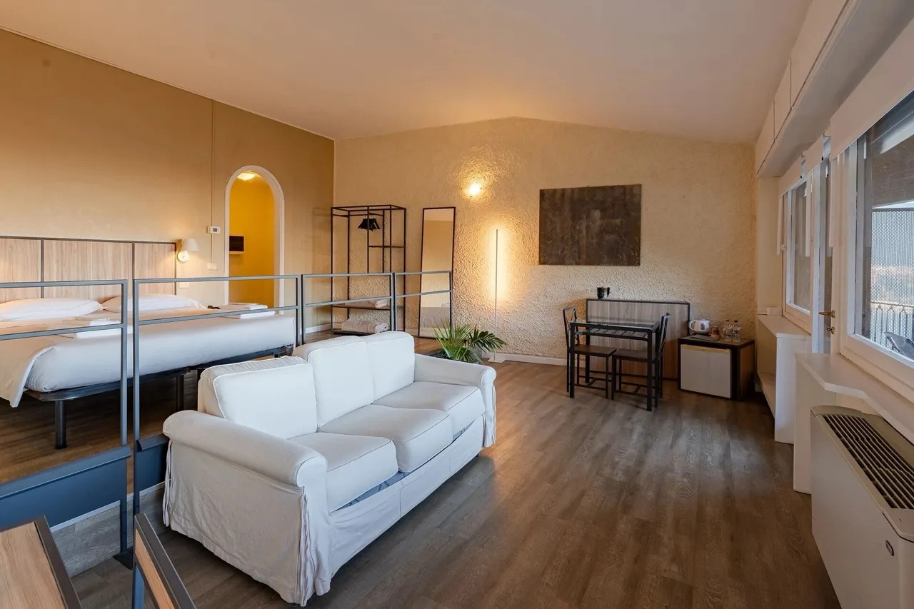Suite at Hotel Il Perlo in Bellagio with white bed, sofa at the foot, wood-style vinyl floor, and classic decor