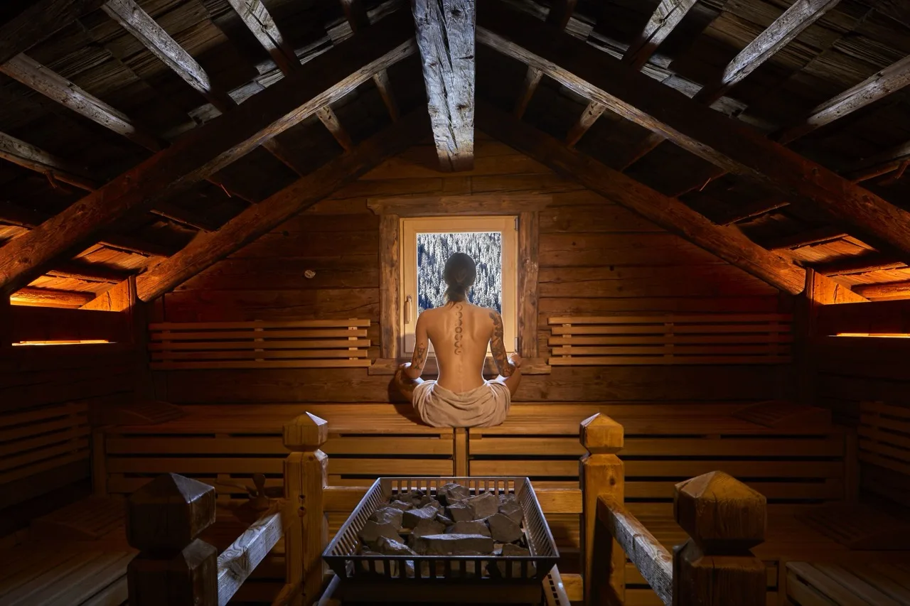 Triangular wooden sauna at Sporthotel Panorama with woman relaxing and looking out the window