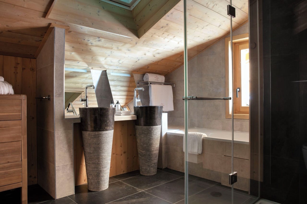 Stylish bathroom at Grandes Rousses Hotel and Spa with wood ceiling stone sinks and glass shower screen