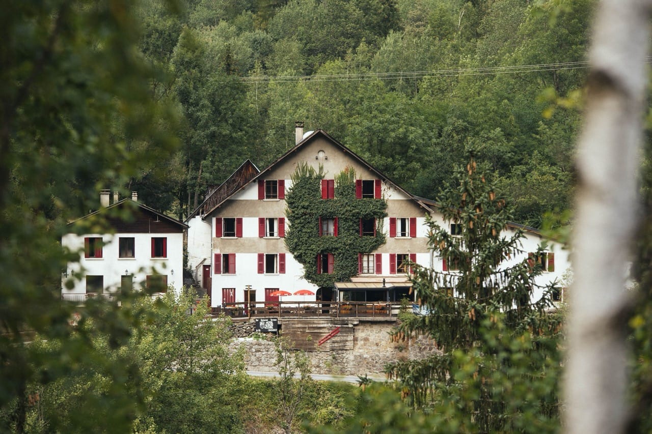 Distant view of Hotel Au Bon Accueil in Les Deux Alpes surrounded by lush greenery and trees