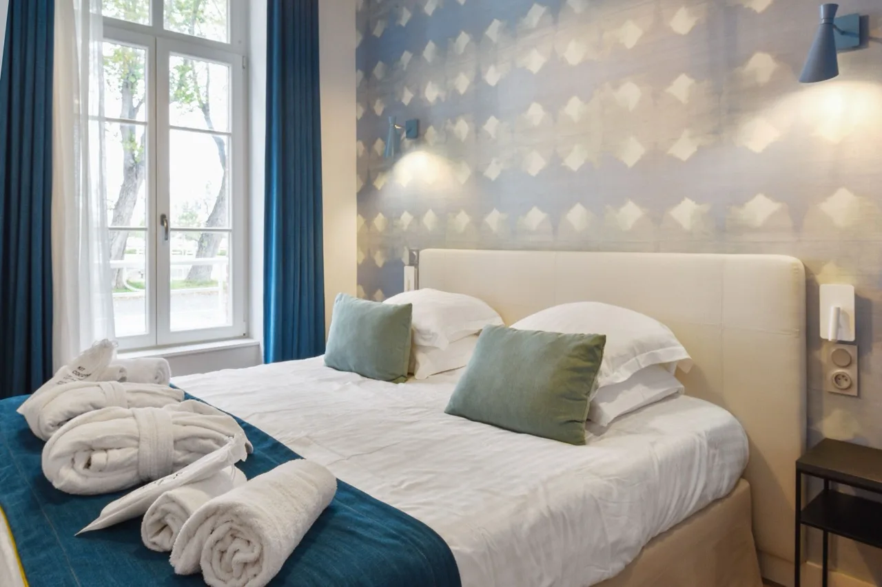 Bedroom featuring a patterned accent wall, large window with royal blue curtains, & a matching bed runner at the foot of the bed