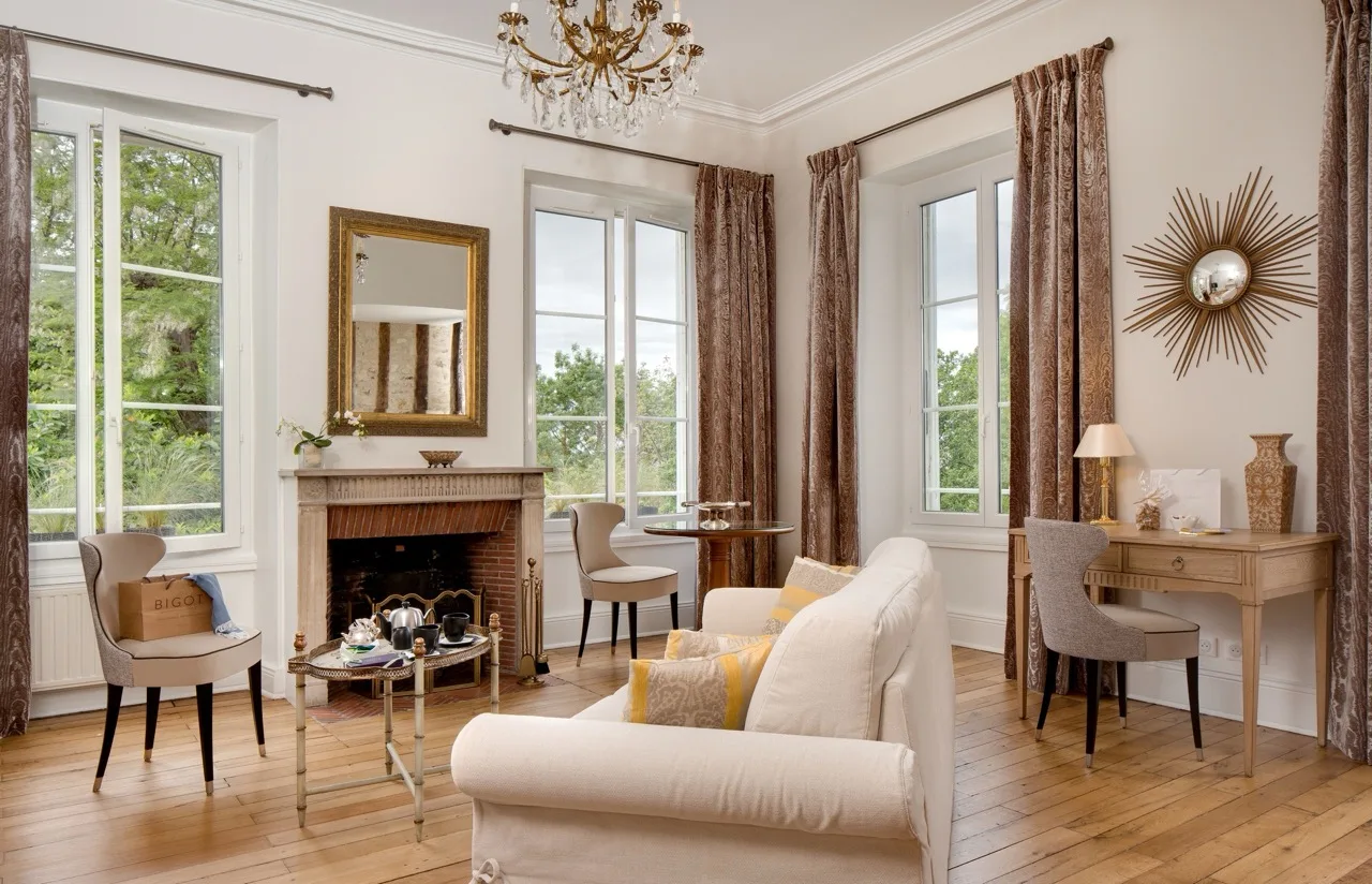 Living room at Le Manoir Les Minimes Amboise with fireplace, white sofa, wooden floor, and large windows with curtains