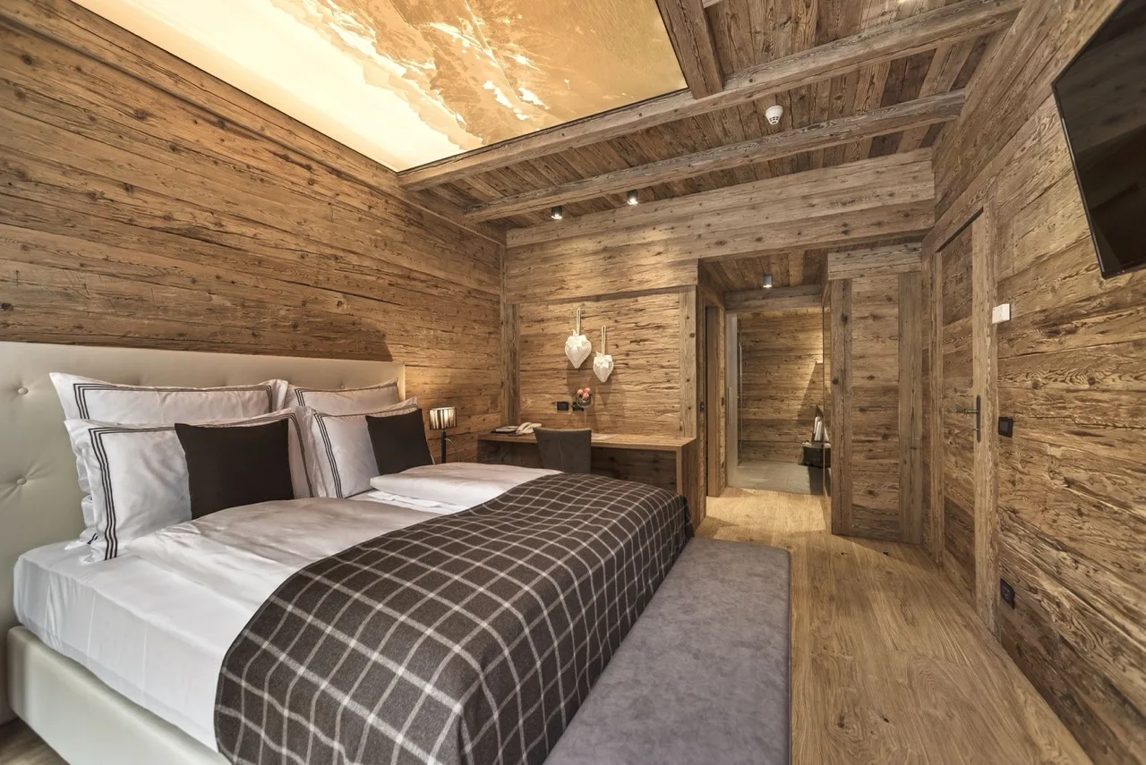 Bedroom at Hotel Cappella in Colfosco with alpine design, wood walls, and modern bedding