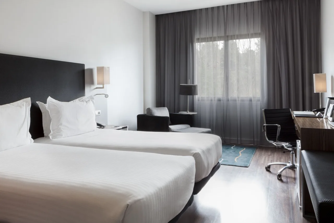 Bedroom at Hotel Palau de Bellavista Girona with two white beds, white walls, and black furnishings