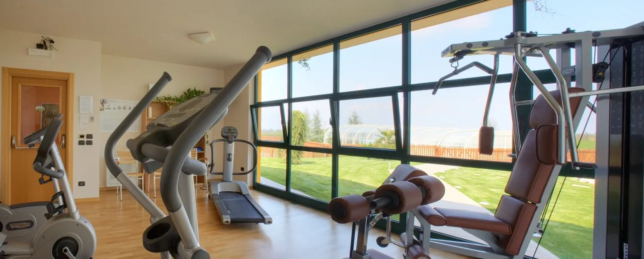 Gym at Lo Scoiattolo Piedmont Bike Hotel with equipment and glass walls overlooking the outdoor scenery