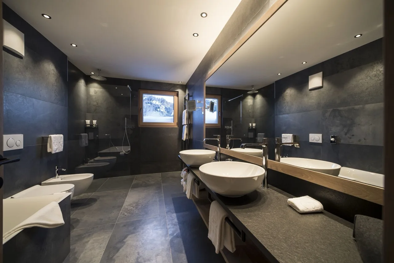 Large bathroom at Hotel Cappella with alpine-modern design, matte black walls, white sinks, toilet, and bathtub