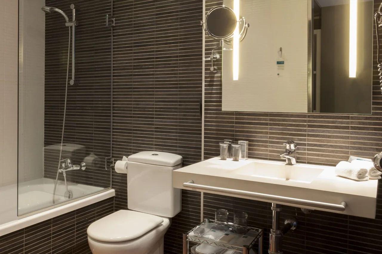Dark-tiled bathroom featuring a white sink, toilet, and bathtub in a modern, minimalist style