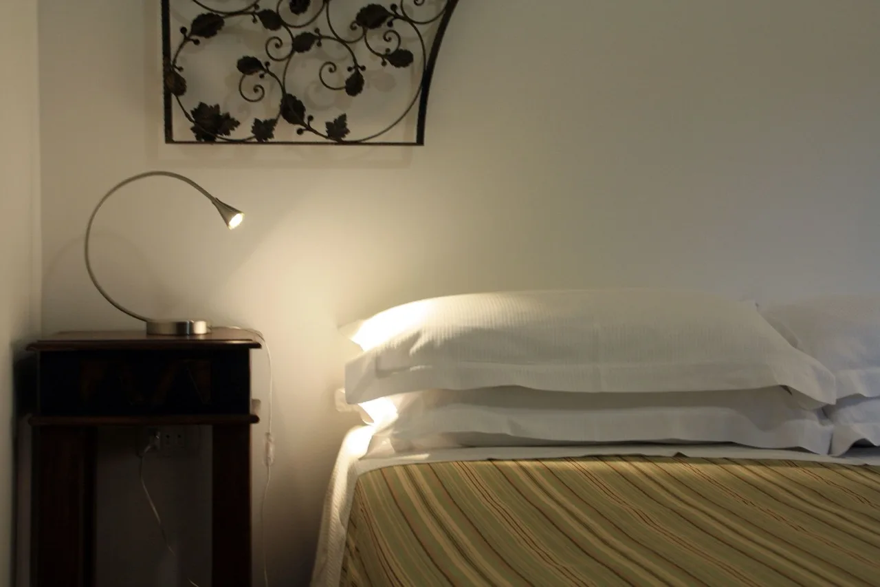 Closeup shot of the head of the bed at B&B Villa Giuliana Arnesano with white walls and a side cabinet