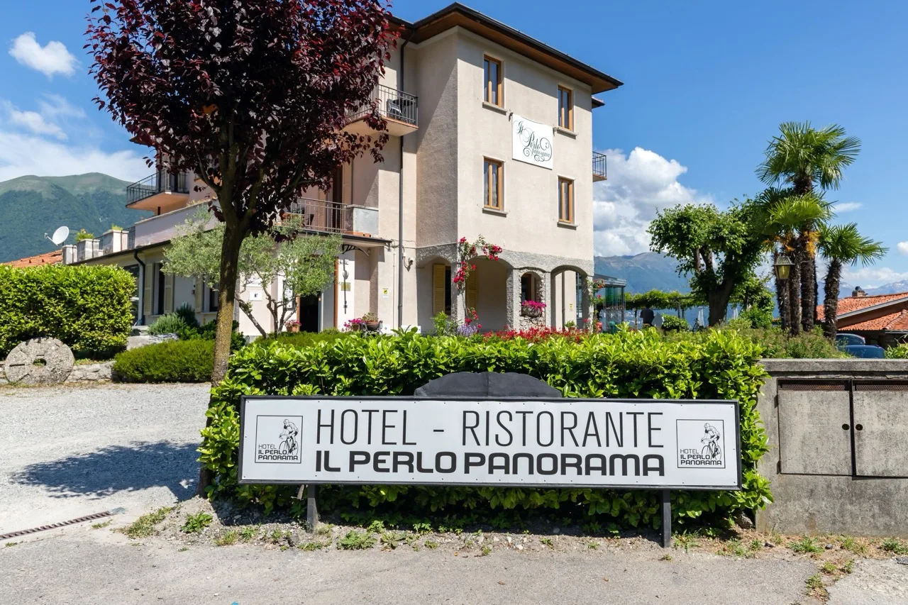 Distant view of Hotel Il Perlo in Bellagio showing the hotel building, signage, and surrounding trees