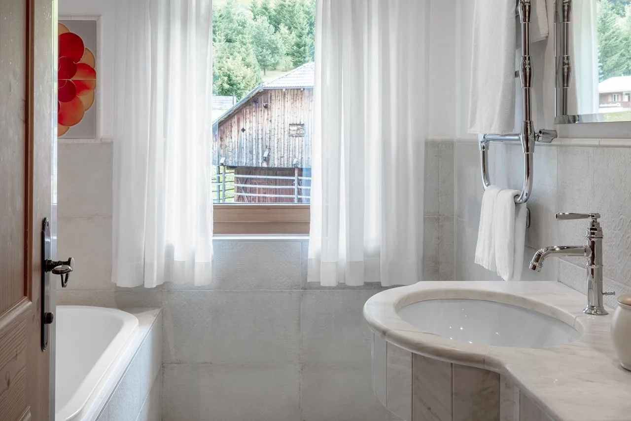 White bathroom at Hotel La Perla in Corvara with large windows and bright natural light