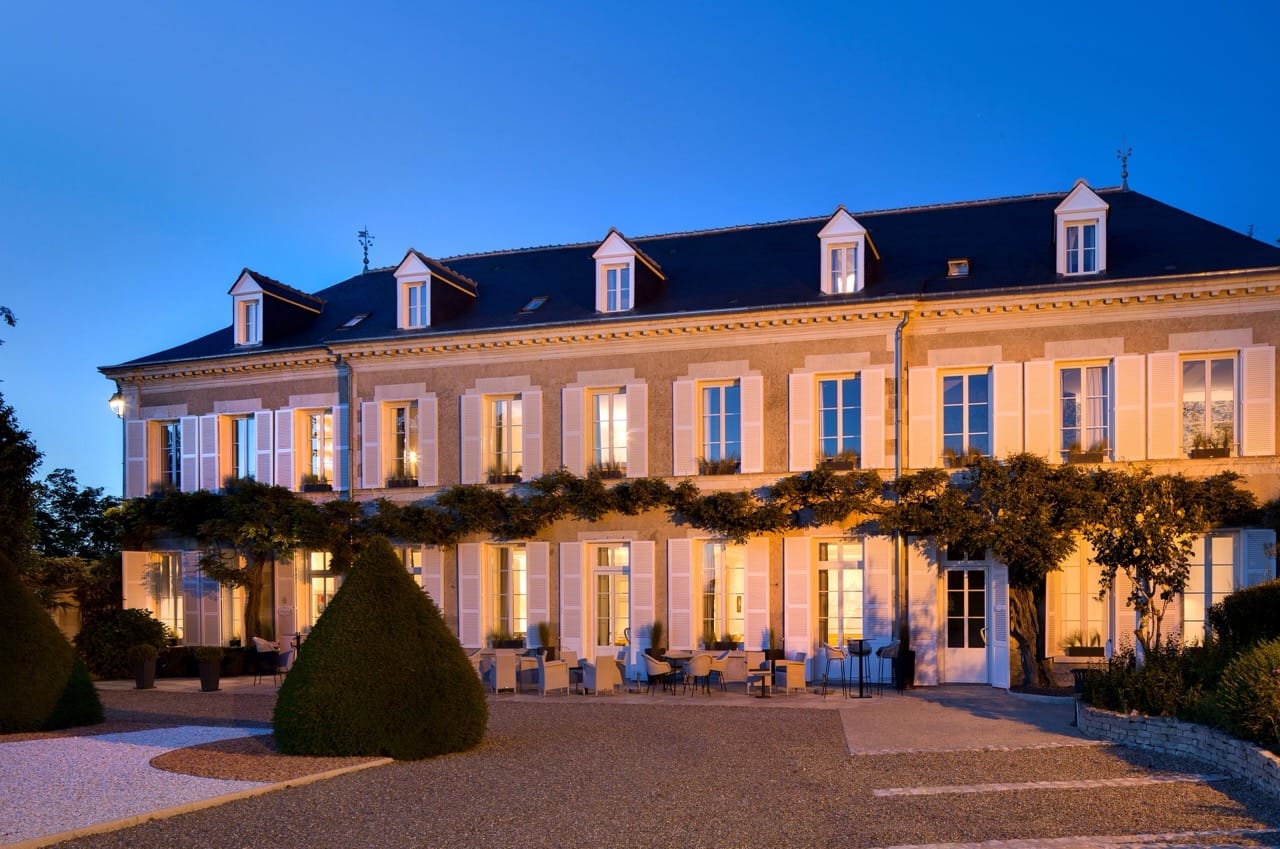 Front view of Le Manoir Les Minimes in Amboise at night with illuminated stone facade and greenery
