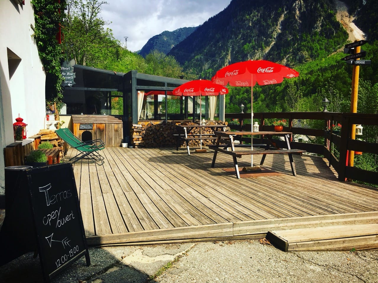 Wooden terrace with red umbrellas picnic benches and mountain view at hotel au bon accueil les deux alpes