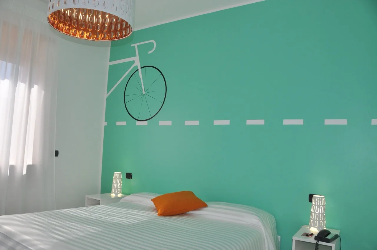 Bedroom at Lo Scoiattolo Piedmont Bike Hotel in Pralormo with pastel green walls, white furniture, and orange accents