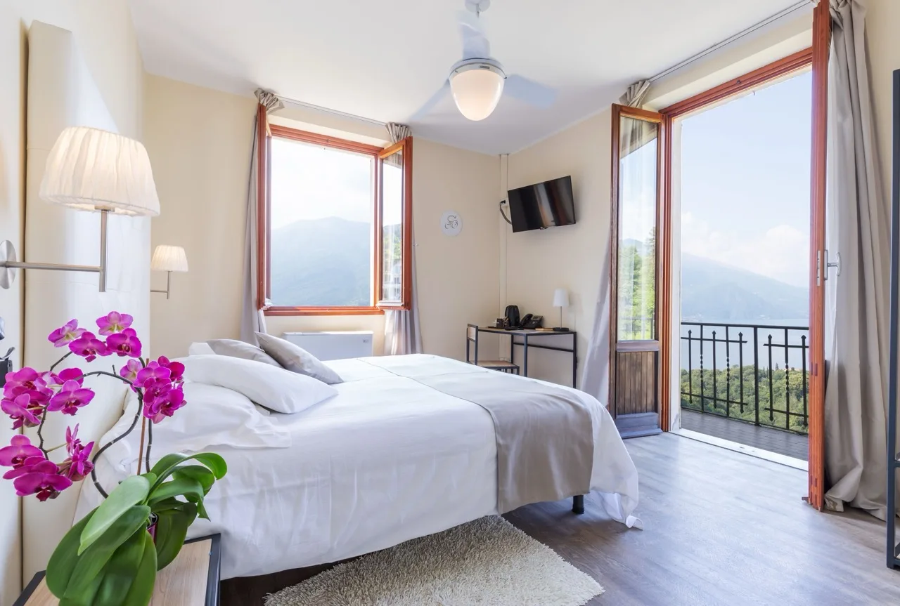 Cosy bedroom at Hotel Il Perlo in Bellagio with a white bed, large window, and two-door entrance to the balcony