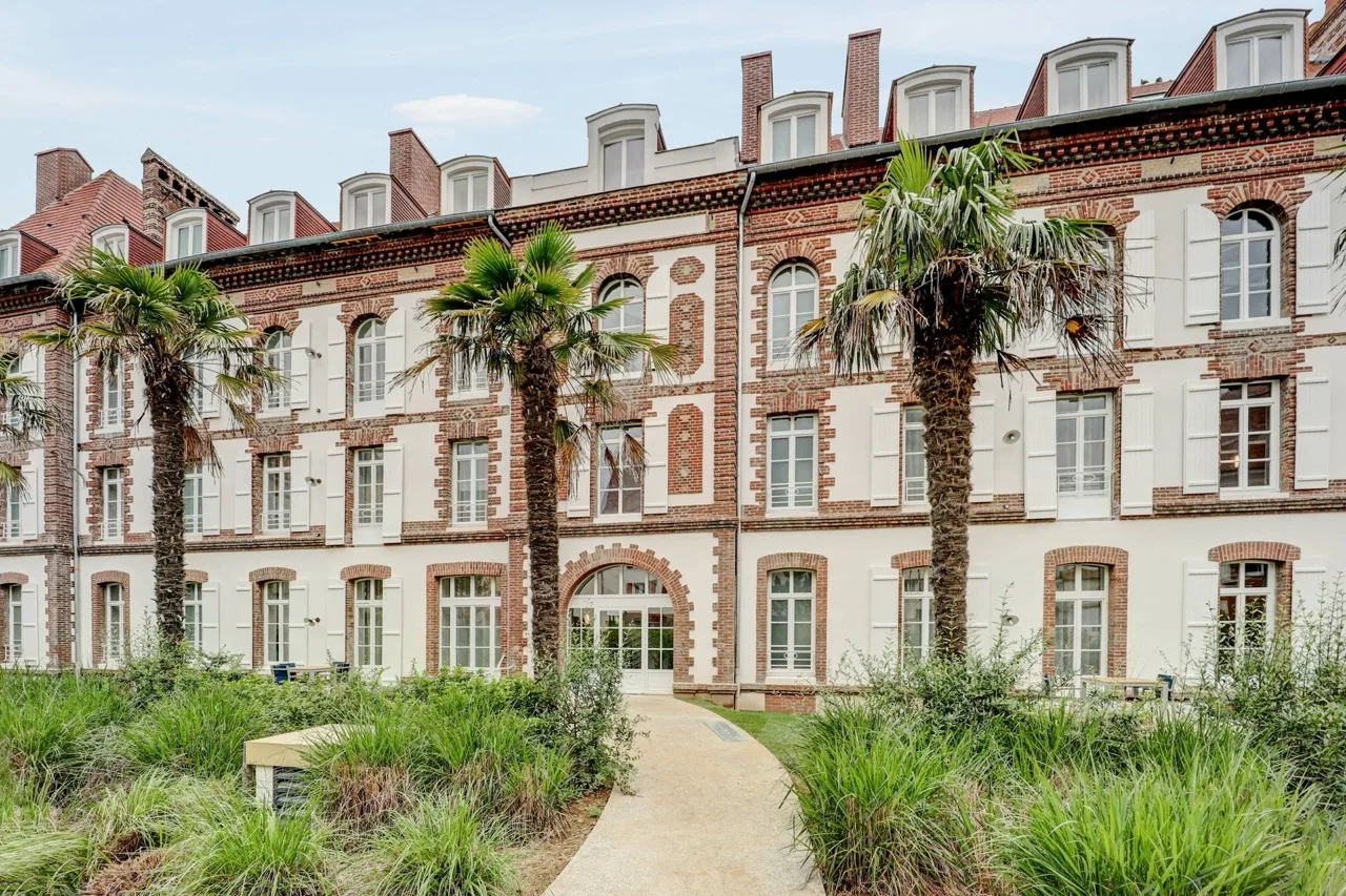 Exterior of Résidence Pierre & Vacances Premium Presqu'Ile de la Touques in Deauville with classic brick and white facade, palm trees