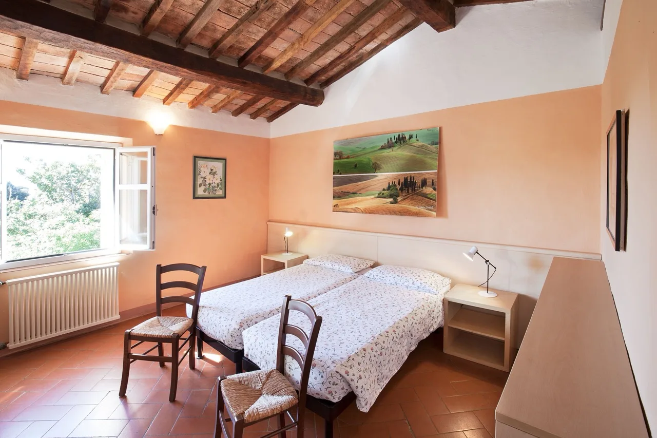 Bedroom at Massa Vecchia with two single beds, side shelves, wooden ceiling, and a large window for natural light