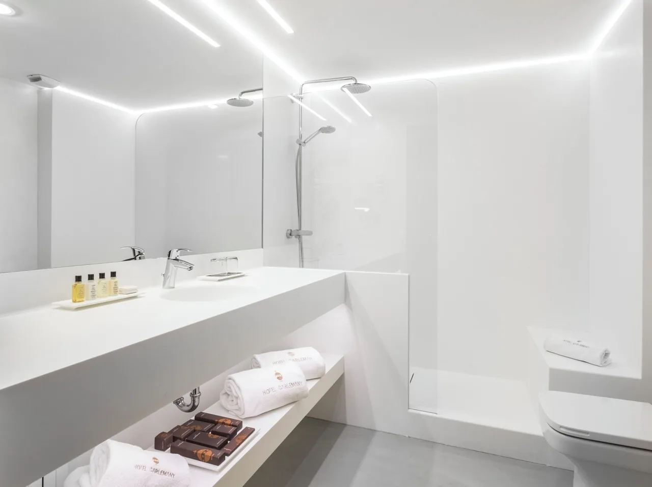 All-white bathroom at Carlemany Girona featuring a large mirror and minimalist, clean design