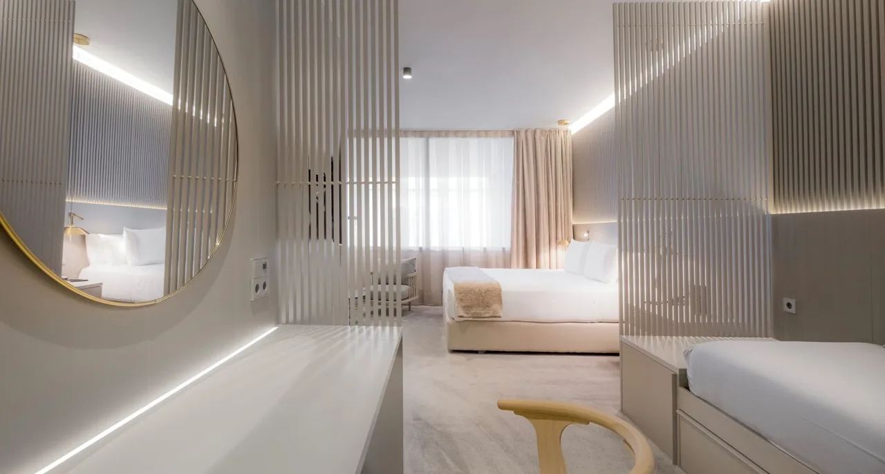 Off-white modern suite at Hotel Carlemany Girona with vanity, chair, and partial view of spacious bedroom