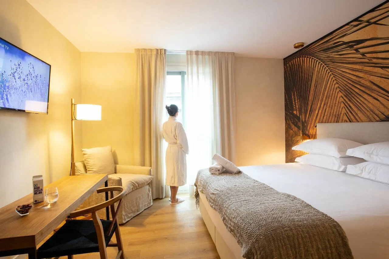 White modern bedroom with large white bed and woman in robe looking out glass sliding door