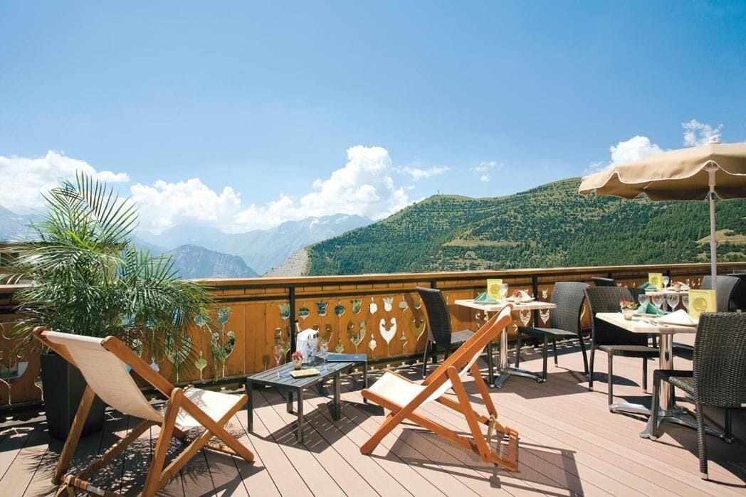 Balcony at Hôtel Le Castillan with comfy seating and tables facing mountain views under clear blue sky