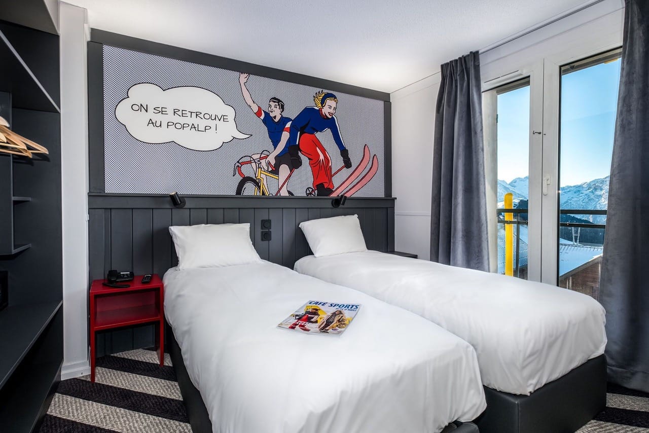 Bedroom at PopAlp with two white single beds, black and white interior, and murals above the beds