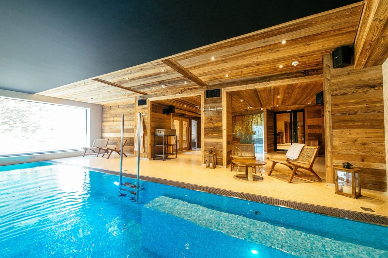 Indoor pool and wooden-designed lounge area at Hotel Le V de Vaujany offering a warm, relaxing space