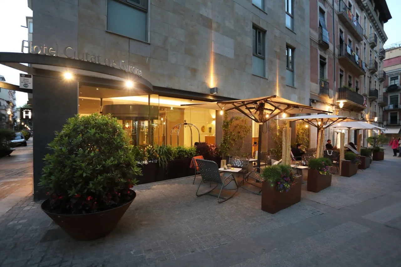 Exterior of Hotel Ciutat de Girona with outdoor tables, chairs, and umbrellas set up in front of the building