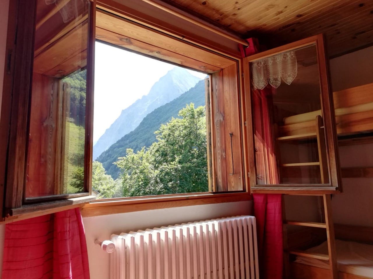 Window view at Gite - Auberge Le Chamois showing mountains, wooden interior, and radiator below