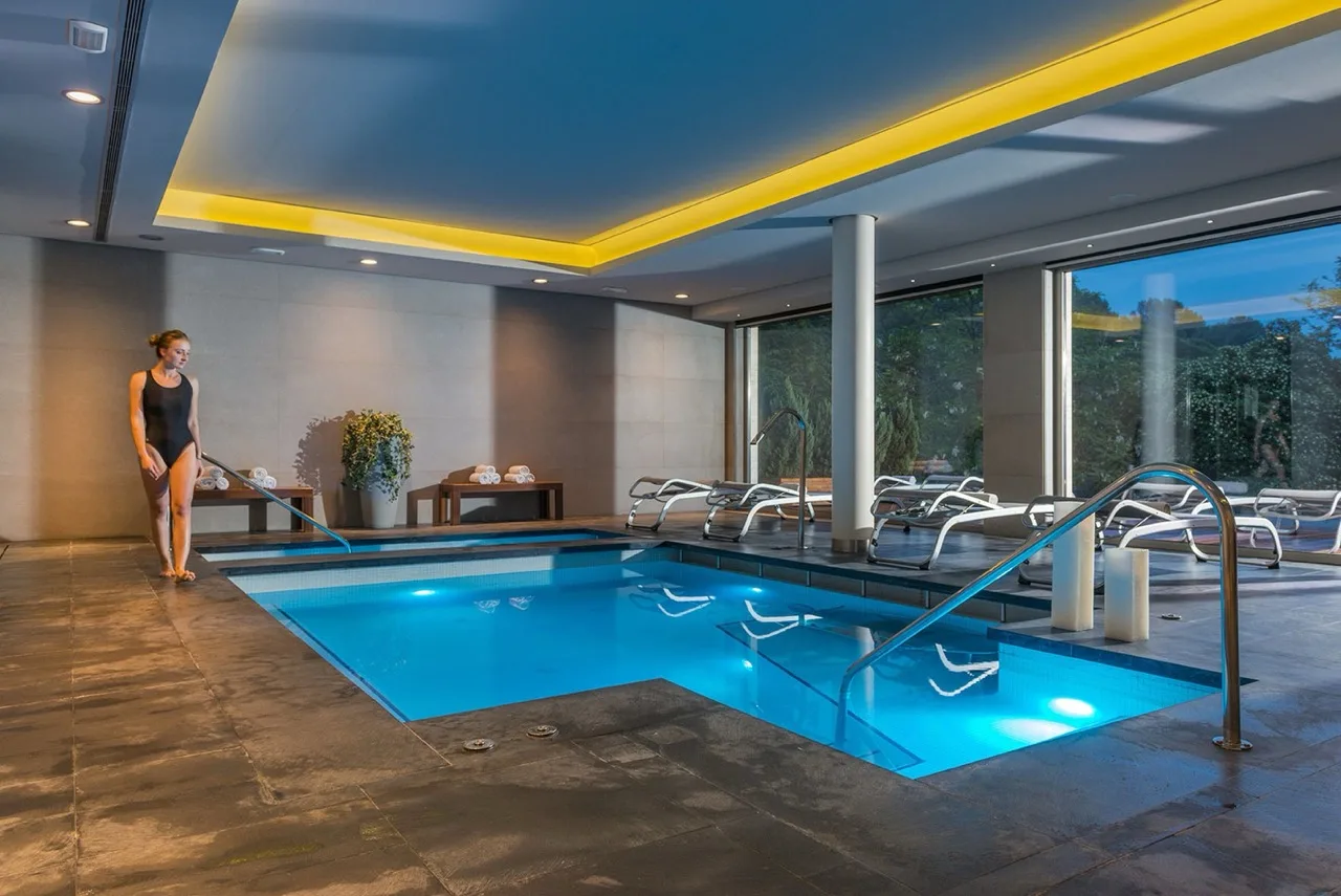 Indoor L-shaped pool at Hotel Santa Marta in Lloret de Mar with large glass walls and serene atmosphere