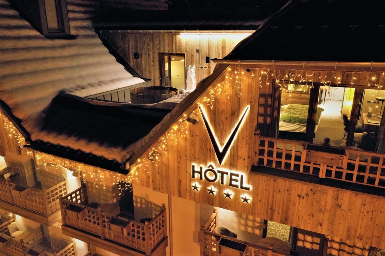 Wooden facade of Hotel Le V de Vaujany at night warmly lit with glowing lights against the dark sky