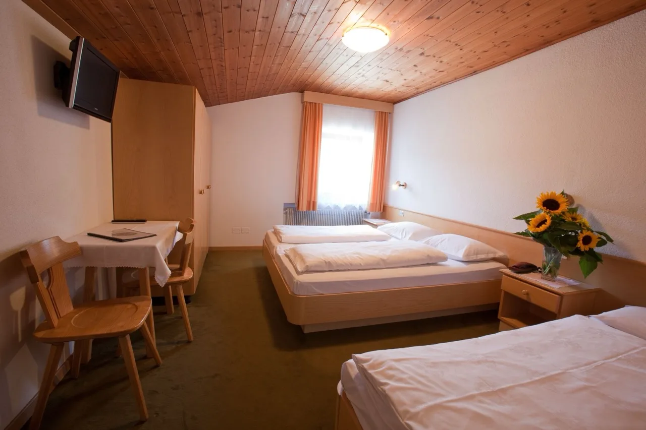 Bedroom at Hotel Ustaria Posta in Badia with three beds, small dining side table, wood and white design