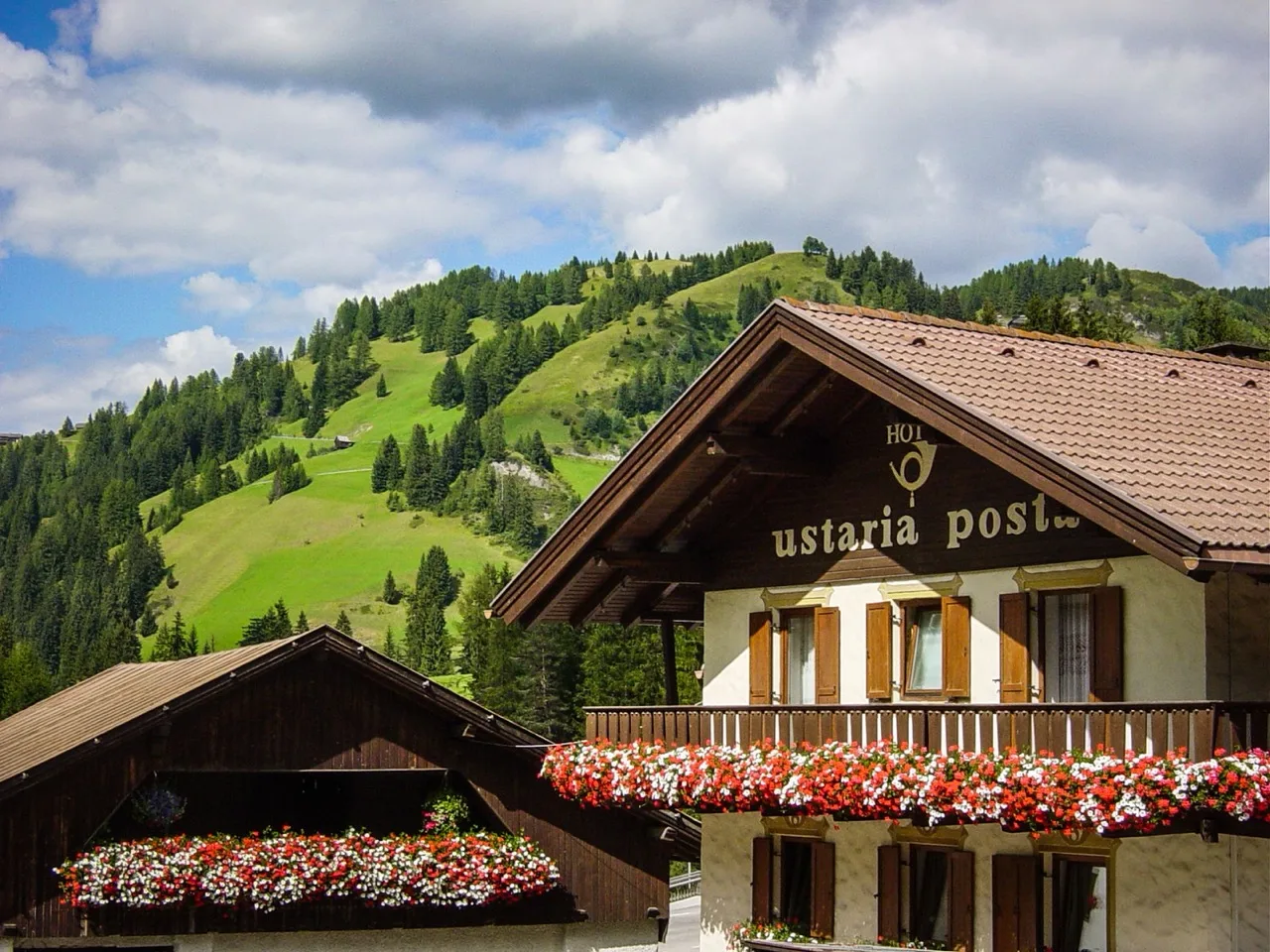 Close-up exterior of upper Hotel Ustaria Posta in Badia showing traditional design with mountain in background