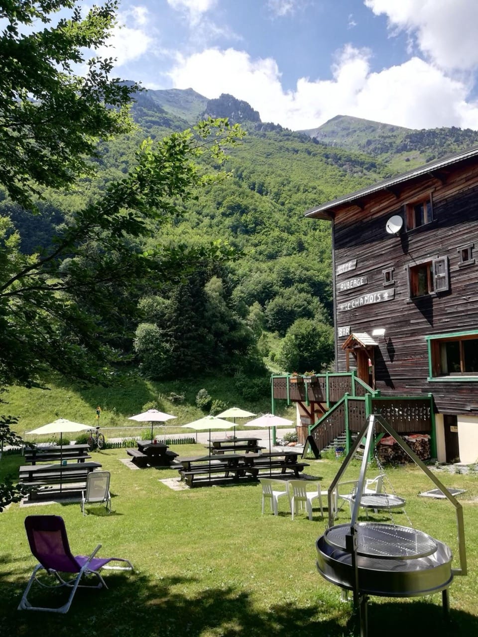 Outdoor area at Gite - Auberge Le Chamois Col d'Ornon with tables umbrellas greenery and mountain backdrop