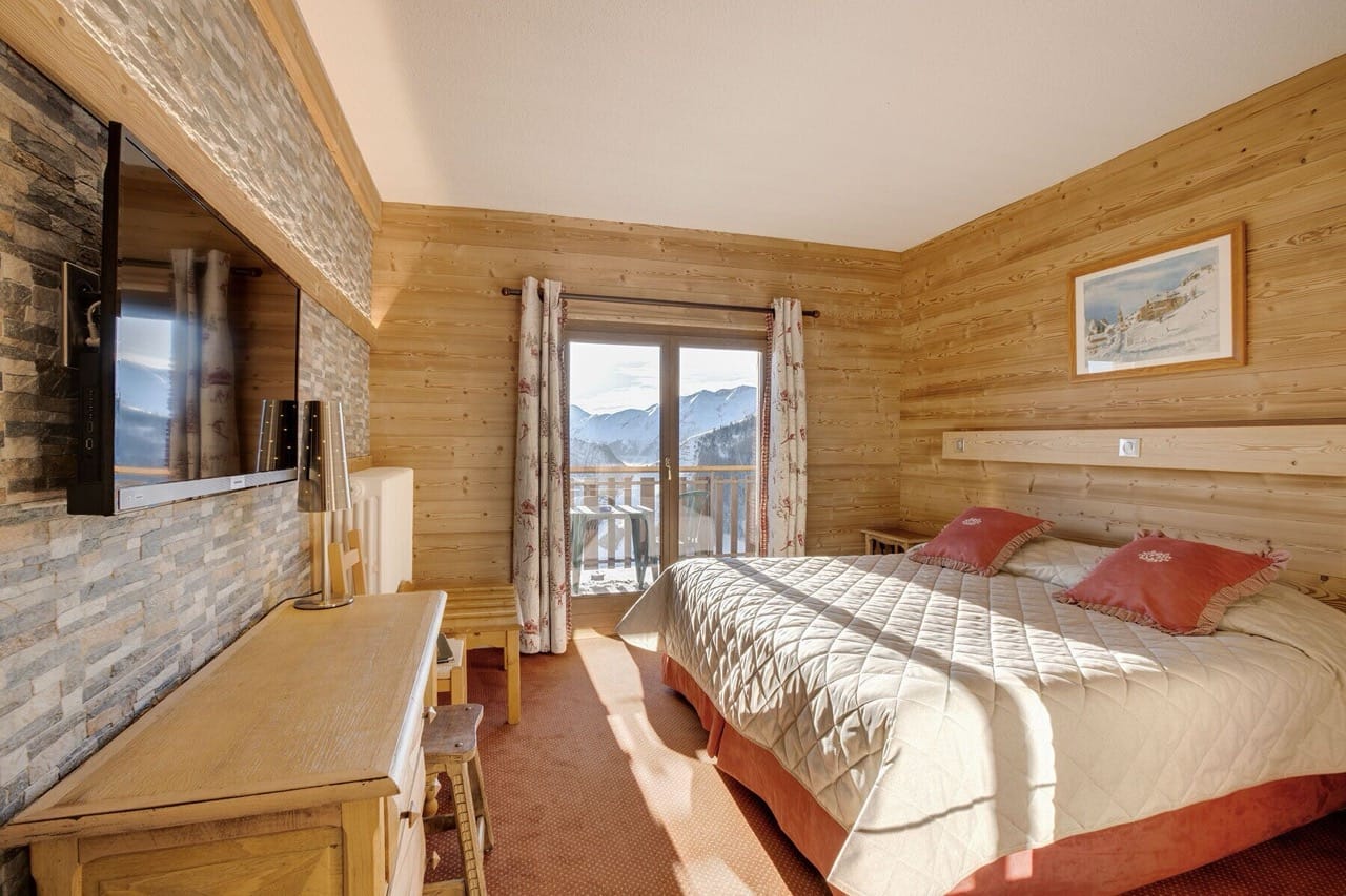 Spacious bedroom at Hôtel Le Castillan with wood accent wall, furniture, and glass door to balcony