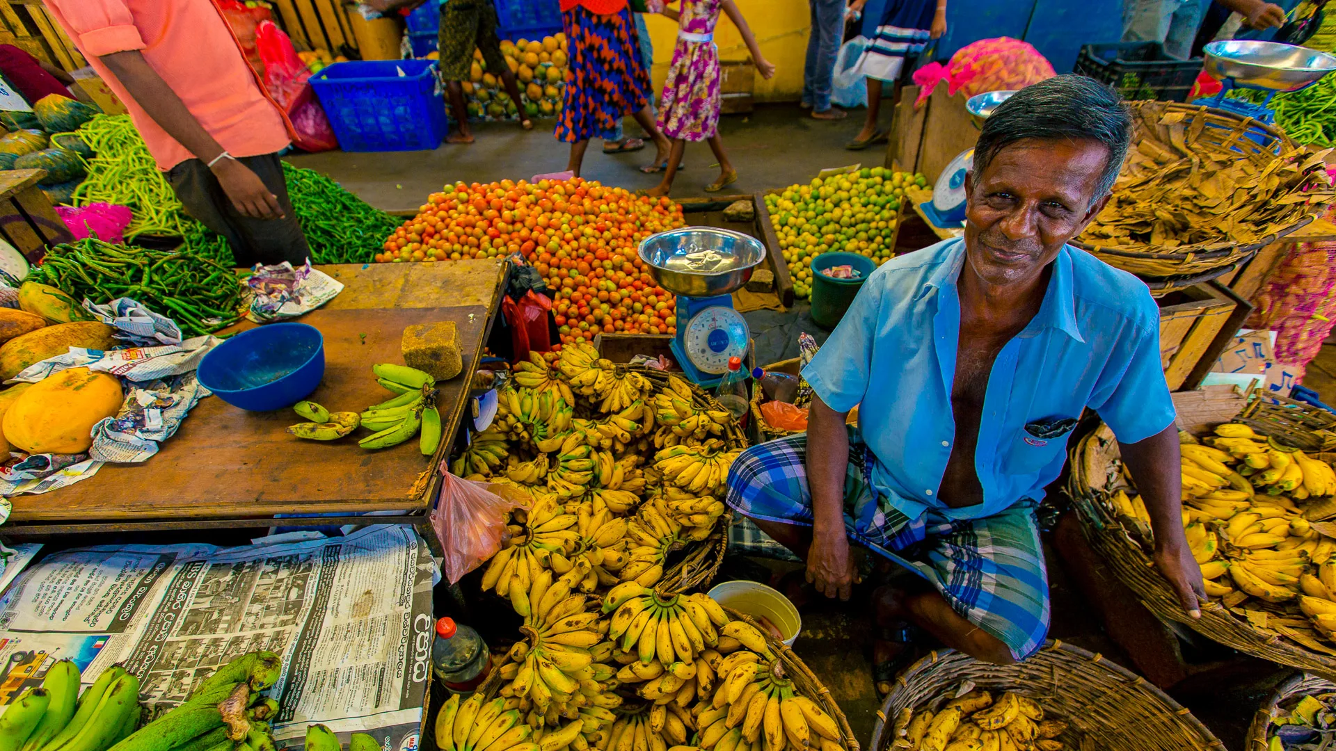 A fruit vendor surrounded by baskets of bananas and other tropical produce in a bustling market